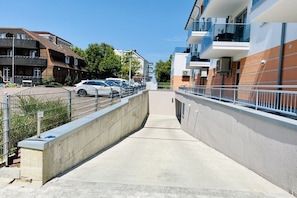 Ein Weg führt zu einem Gebäude mit modernem Design, mit Balkonen und einem Parkplatz mit Autos.