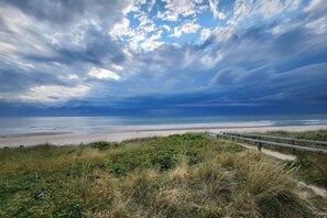 Eine Küstenlandschaft mit Strand, grasbewachsenen Dünen und einem Holzsteg.
