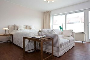 Ein Schlafzimmer mit einem Bett, einem Nachttisch, einer Lampe, einem Fenster und einem Sessel.