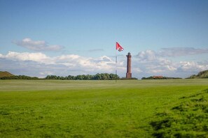 Klarer Himmel mit einer Fahne an einem Mast, einem Turm und einem grünen Feld.
