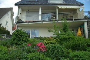 A two-story residential building with a balcony, surrounded by lush greenery and flowering plants. - Stentenbach in the Aggertal (Engelskirchen-Ründeroth)