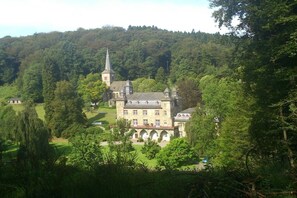 A large, historic building with a prominent tower, surrounded by lush greenery and a hilly landscape. - Stentenbach in the Aggertal (Engelskirchen-Ründeroth)