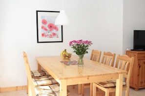 Ein Essbereich mit Holztisch, Stühlen, einer Blumenvase, Obstschale und einem gerahmten Bild an der Wand.