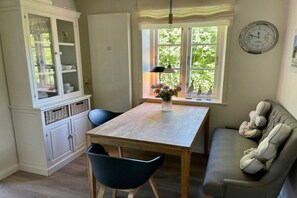 A dining area with a wooden table, chairs, a cabinet with glass doors, a window with a view of greenery, and a clock on the wall. - "Oyster" in the house Clarinet (Nebel)
