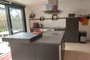 A modern kitchen with a central island, a microwave, and a trash bin. - Holiday home with 2 bedrooms (Butjadingen - Burhave)