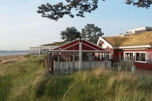 Ein Küstengebäude mit rotem Dach, umgeben von Gras und Bäumen, mit Blick auf das Meer.