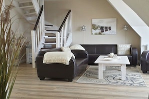 Ein Wohnzimmer mit einem dunklen Sofa, einem weißen Couchtisch und einer Treppe mit weißen Geländern.