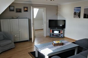A living room with a sofa, a coffee table, a TV, and a bookshelf. - House Pirate's Nest Apartment 5 (Borkum)