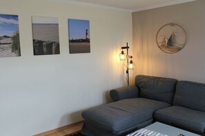 A living room with a grey sofa, a coffee table, and wall art depicting coastal scenes. - House Pirate's Nest Apartment 5 (Borkum)