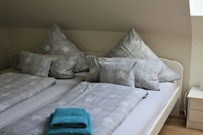 A double bed with grey bedding and star-patterned pillows, a blue towel on the bed, and a white bedside table. - House Pirate's Nest Apartment 5 (Borkum)