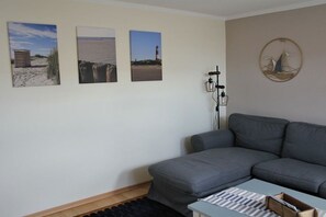 Ein Wohnzimmer mit einer grauen Couch, einem kleinen Tisch und drei gerahmten Bildern an der Wand.