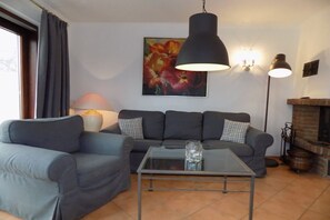 A living room with a sofa, a glass coffee table, a lamp, and a fireplace. - House Oland Holiday Apartment 7 (Wenningstedt)