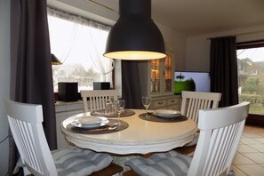 A dining area with a round table, white chairs, and a black pendant light. - House Oland Holiday Apartment 7 (Wenningstedt)