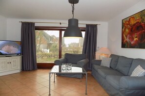 A living room with a television, grey sofa, and a table with glasses. - House Oland Holiday Apartment 7 (Wenningstedt)