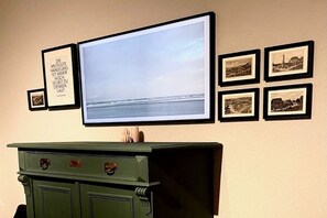 Ein an der Wand befestigter Fernseher mit einem gerahmten Zitat und vier gerahmten Fotografien darunter.