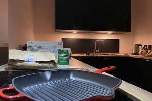 Eine Küche mit einem Herd, einer roten Pfanne, einer Tüte Lebensmittel und einer Kiste Gemüse.