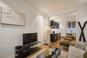 A modern living room with a flat-screen TV, a coffee table, and a sofa. There is a kitchen area with cabinets and a dining table. - Charming Apartment Champs Elysees Montaigne (Paris)