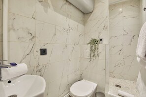 A bathroom with a marble wall, a white sink, a toilet, and a shower area. - Charming Apartment Champs Elysees Montaigne (Paris)