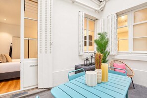 Une pièce avec un lit, une table et des chaises, une plante et une fenêtre avec des volets.