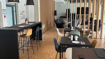A modern office space with a long communal table, individual seating, and a partitioned area with a large screen.