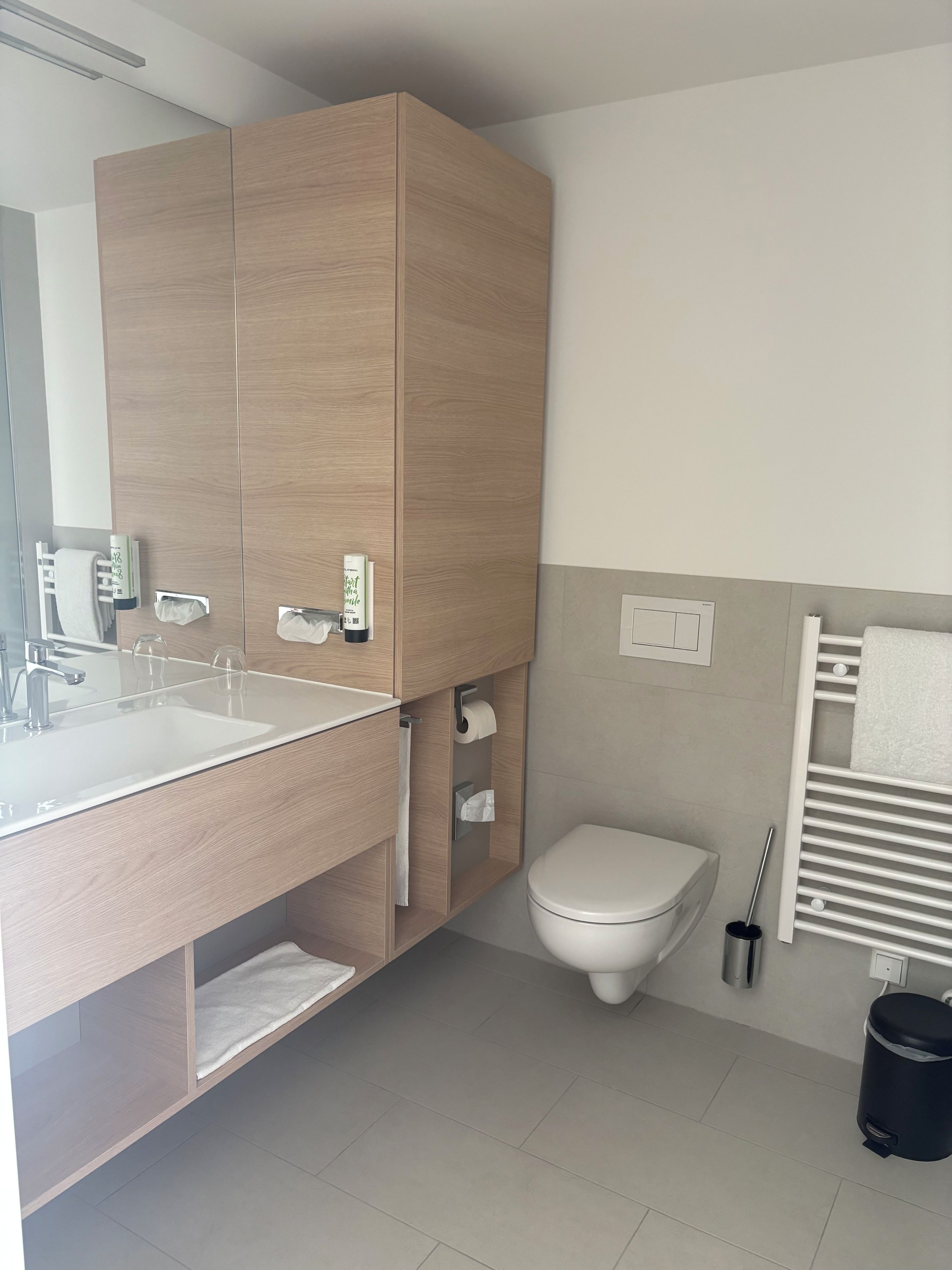 A modern bathroom with a wooden vanity, a sink, a toilet, and a towel rack.