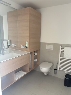 Um banheiro moderno com toucador de madeira, pia, vaso sanitário e porta-toalhas.