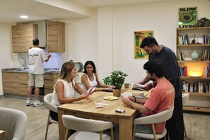 A group of people engaged in a card game at a wooden table in a modern kitchen with wooden cabinets and a bookshelf. - Lemon Tree Hostel (Málaga)