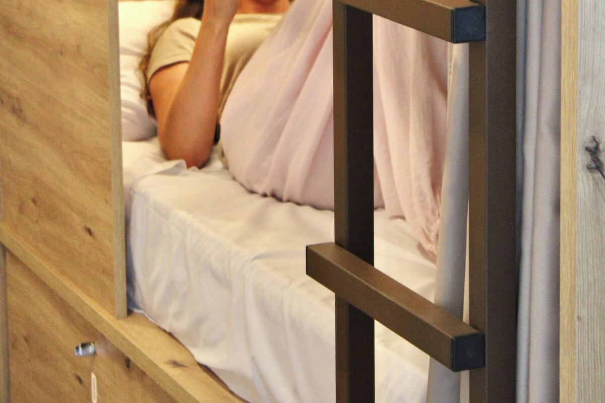 A wooden bunk bed with a ladder, a person reading a book, and a white pillow.