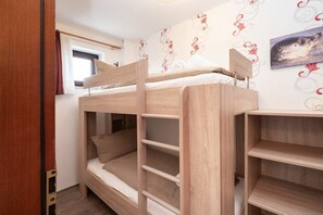 A bunk bed with a wooden frame and a headboard, a window with curtains, and a wall with a floral pattern. - Quarter 6 Apartment 12 (Büsum)