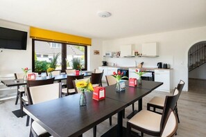A modern dining area with a long table, chairs, and a kitchen in the background. - Quarter 6 Apartment 12 (Büsum)
