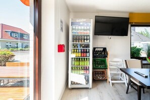 Quarto com máquina de bebidas, televisão de tela plana e área de estar externa.