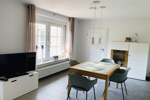 Una sala de estar moderna con un televisor de pantalla plana, una mesa de comedor con sillas, una chimenea y un ventanal con cortinas.