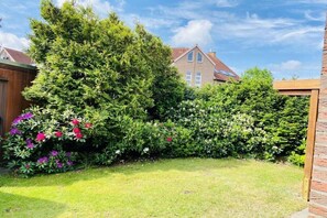 A residential garden with a lawn, various shrubs, and a wooden fence. - Holiday apartment with 2 bedrooms (Cuxhaven)