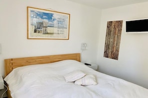 A hotel room with a wooden bed, a framed picture on the wall, a television, and a power outlet. - Holiday apartment with 2 bedrooms (Cuxhaven)