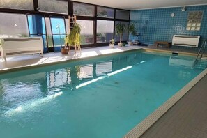 An indoor swimming pool with clear water, surrounded by windows, potted plants, and a bench. - Tiny Atelier Bad Harzburg (Bad Harzburg)