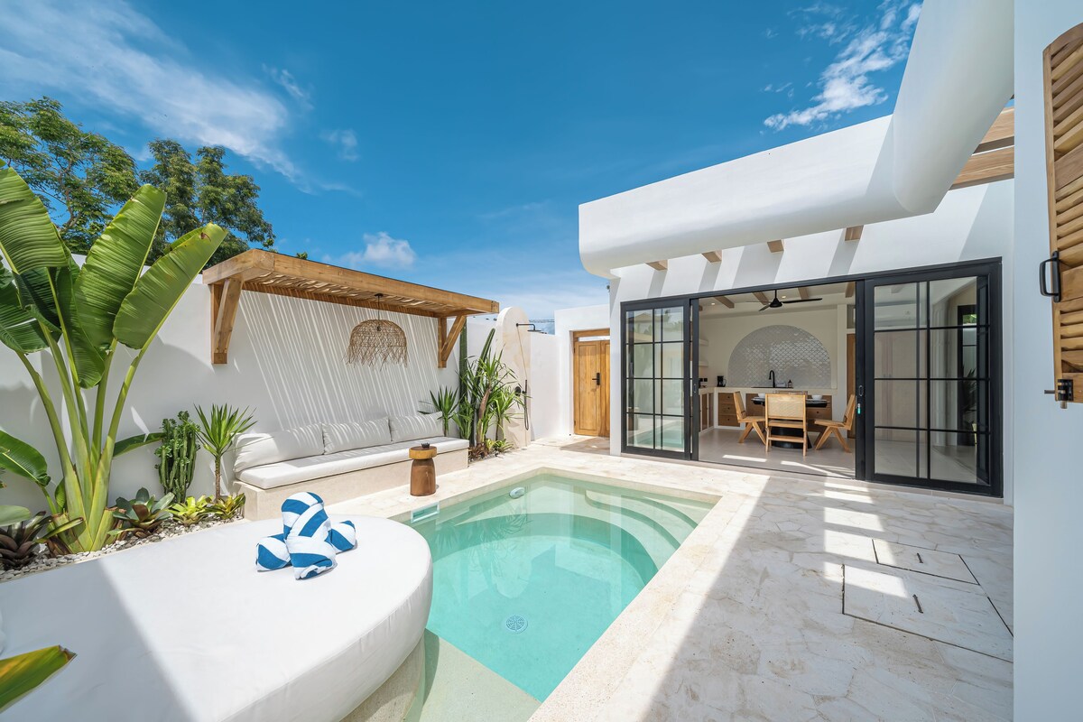A modern outdoor pool area with a white lounge chair, a wooden pergola, and a dining area with a glass door.