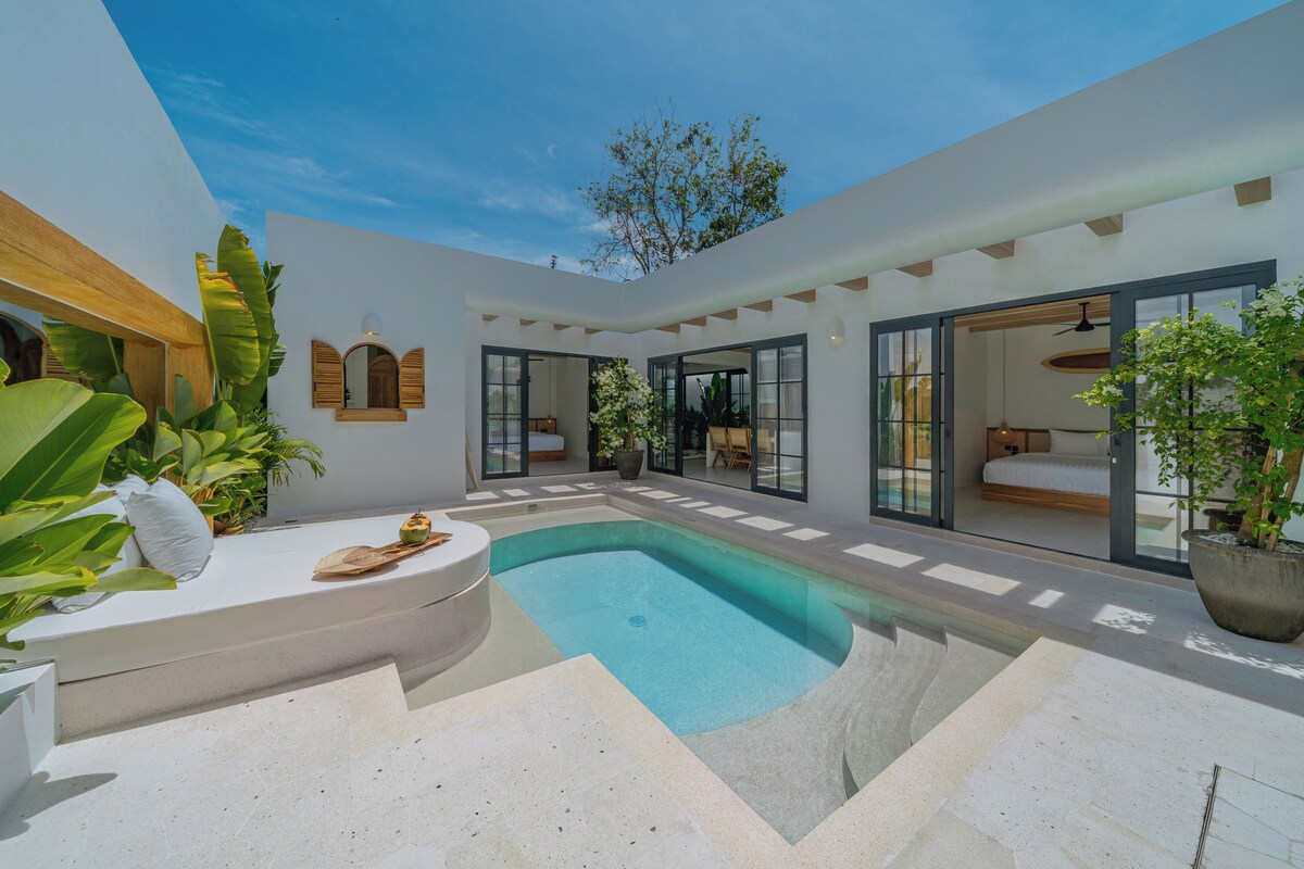 A modern outdoor pool area with a clear blue pool, surrounded by a white building with large glass doors and windows.