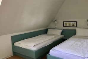Ein kleines Zimmer mit einem Einzelbett, geneigter Decke, einem Nachttisch und einer Wandlampe.