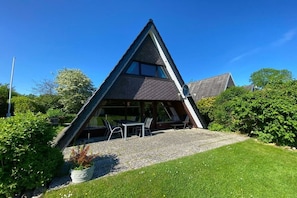 A triangular building with a sloped roof, a patio with outdoor seating, and a gravel pathway leading to the entrance. - Holiday home in Damp with barbecue and Wi-Fi (Damp)