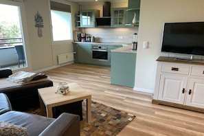 A modern kitchen with a built-in oven, a dining area with a table and chairs, and a television on a cabinet. - Holiday apartment in Damp with swimming pool (Damp)