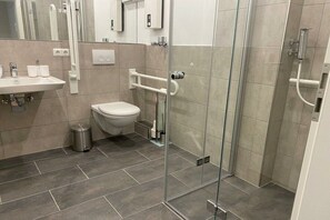 Een moderne badkamer met een douchecabine van glas, een wit toilet en een wastafel met een afvalbak.
