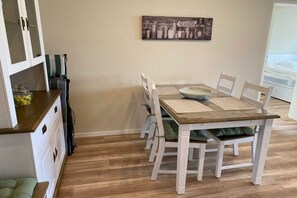 A dining area with a wooden table and white chairs, a kitchen area with cabinets and a countertop, and a wall-mounted artwork with the word 'SEASIDE'. - Holiday apartment in Damp with swimming pool (Damp)