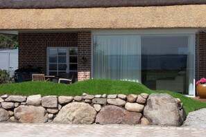 Een gebouw van baksteen met rieten dak, een stenen muur en een terras met buitenmeubilair.
