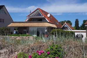 Een huis met een schuin dak, een schotelantenne en een stenen muur op de voorgrond.