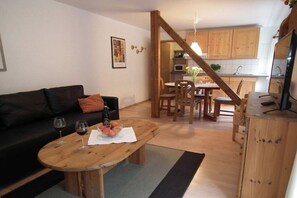 A living room with a wooden coffee table, a black sofa, and a dining area with wooden chairs and a table. - in the holiday home Nexö - 1 bedroom (Ilsenburg)