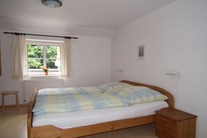 Een enkel bed met houten frame, een klein nachtkastje, een radiator en een raam met gordijnen.