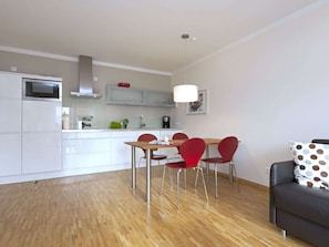 Eine moderne Küche mit weißen Schränken, einem Esstisch mit roten Stühlen und einem grauen Sofa mit einem gepunkteten Kissen.