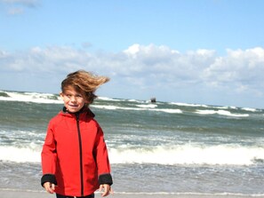Eine Person steht an einem Strand, im Hintergrund sind Wellen zu sehen.