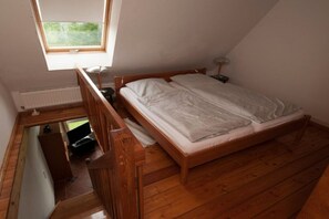 A bedroom with a wooden bed, a nightstand, a desk, and a window. - Maisonette holiday apartment (6) (Wurster Nordseeküste)