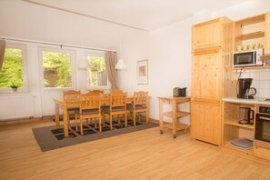 Ein Zimmer mit Esstisch und Stühlen, eine Küche mit Holzschränken, einer Mikrowelle und einem Wasserkocher.